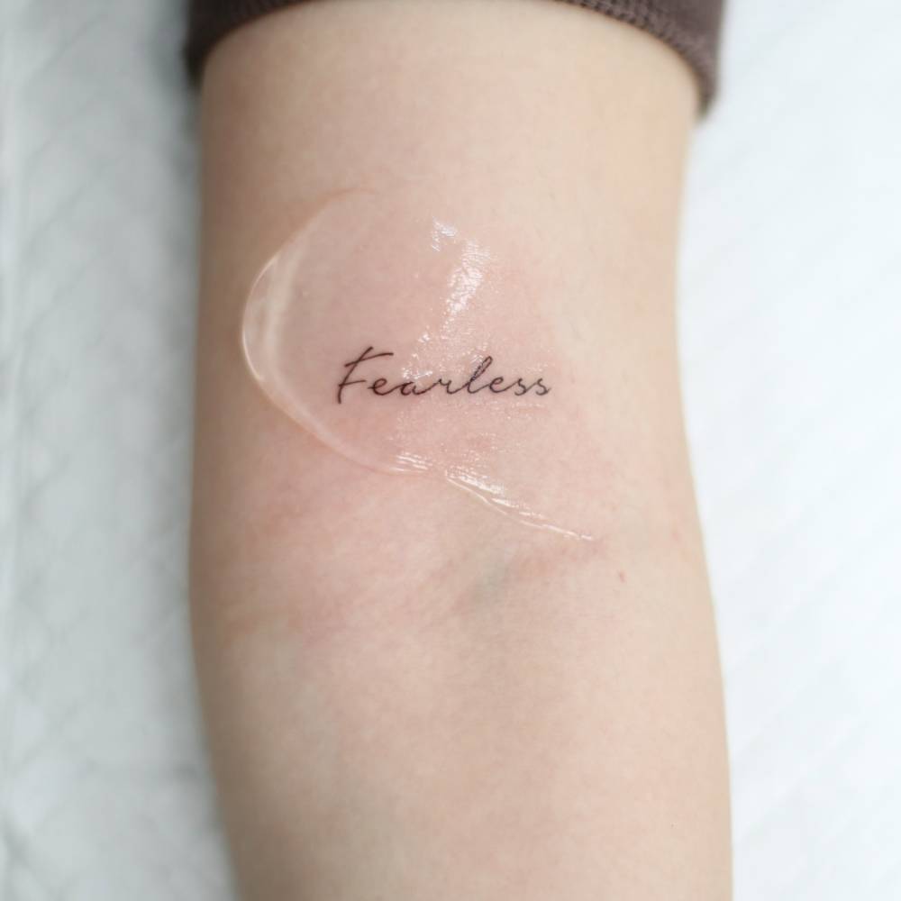 Handwritten font word "fearless" tattoo located on the bicep.
