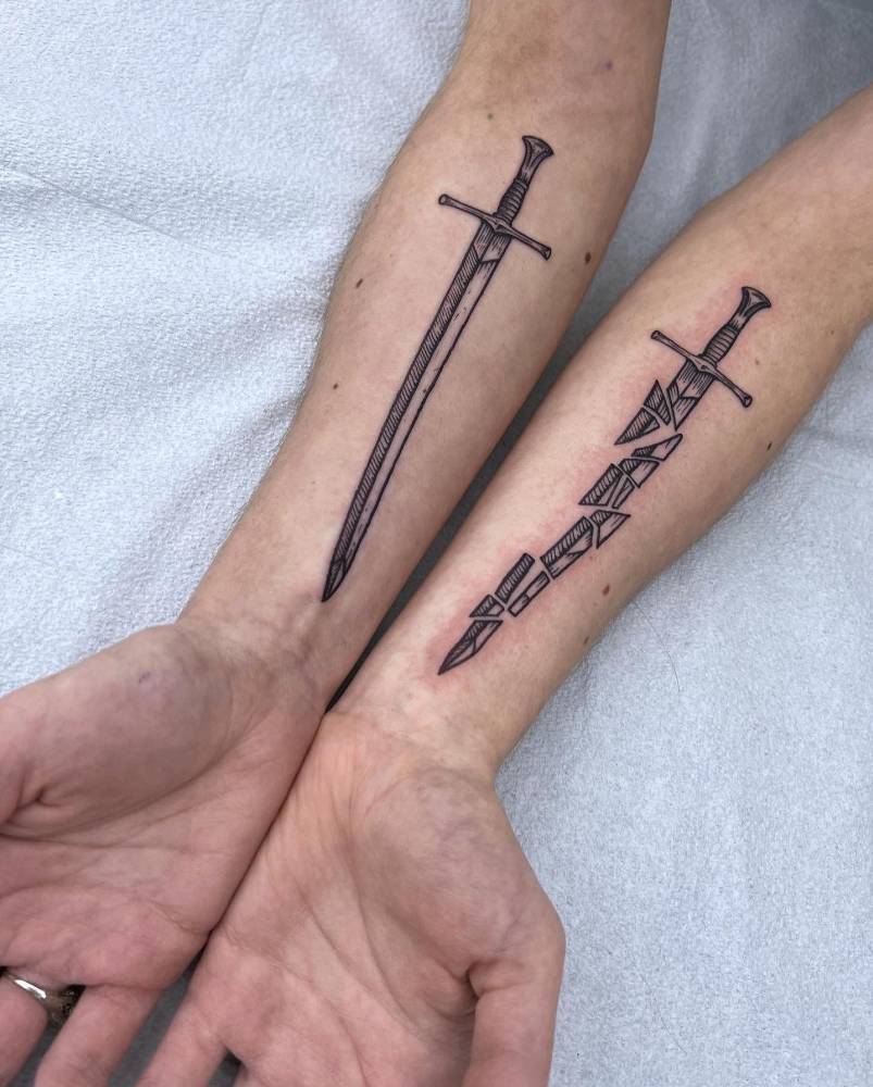 Individual matching sword and broken sword tattooed on the inner forearms.