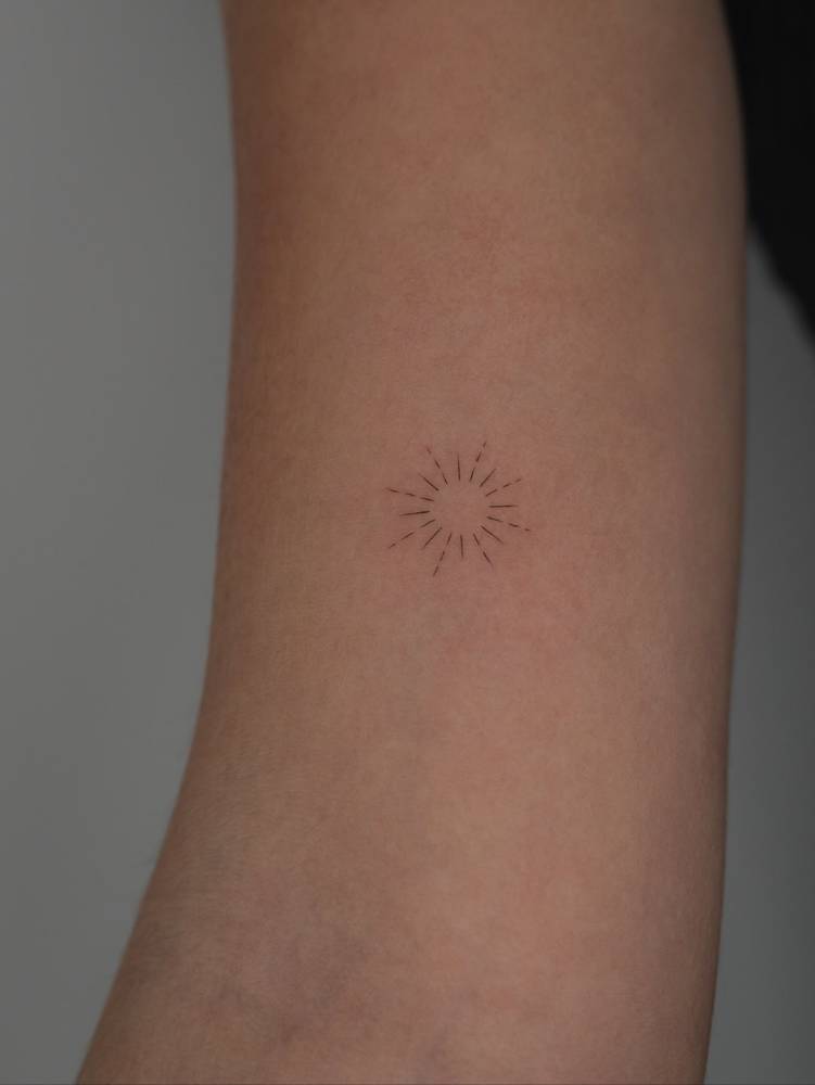 Minimalistic style little sun tattoo placed on the inner arm.