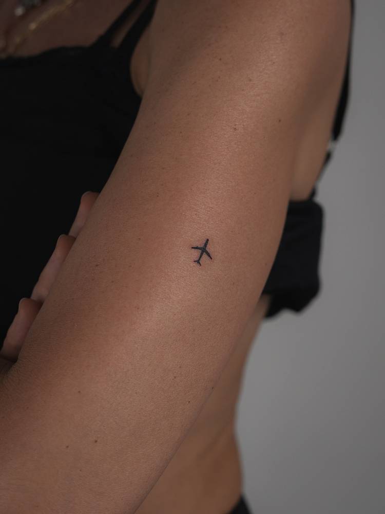 Tiny minimalistic airplane tattoo located on the upper arm.