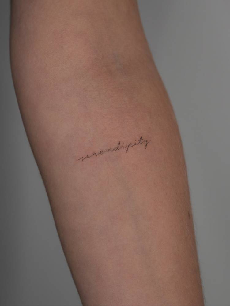 Word "serendipity" in handwritten font tattooed on the inner forearm.