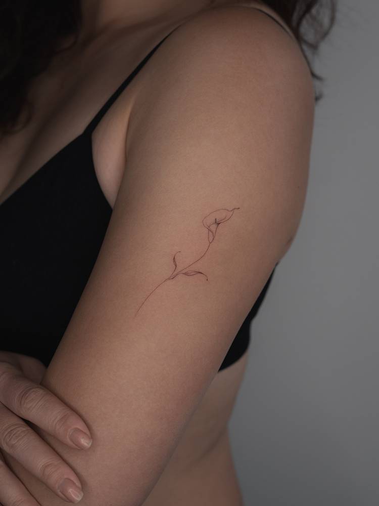 Single needle calla lily tattoo located on the upper arm.