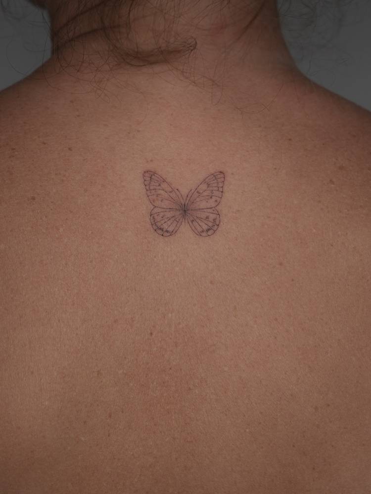 Little butterfly tattoo placed on the upper back, fine line style.