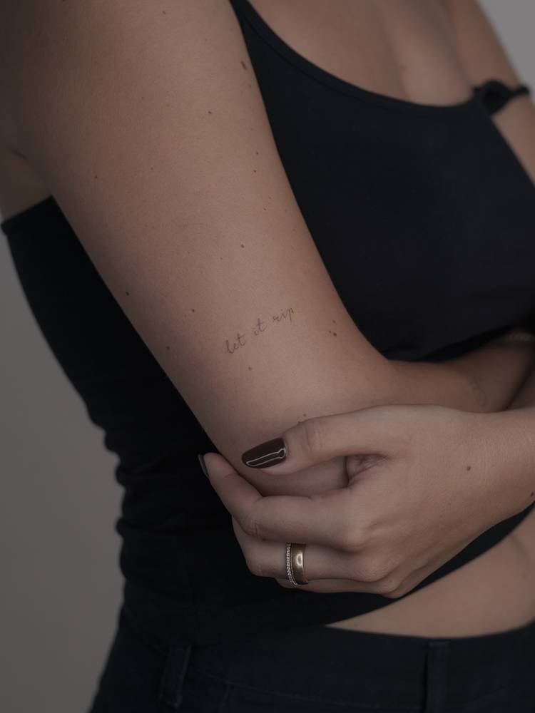 "Let it rip" lettering tattoo located on the upper arm.