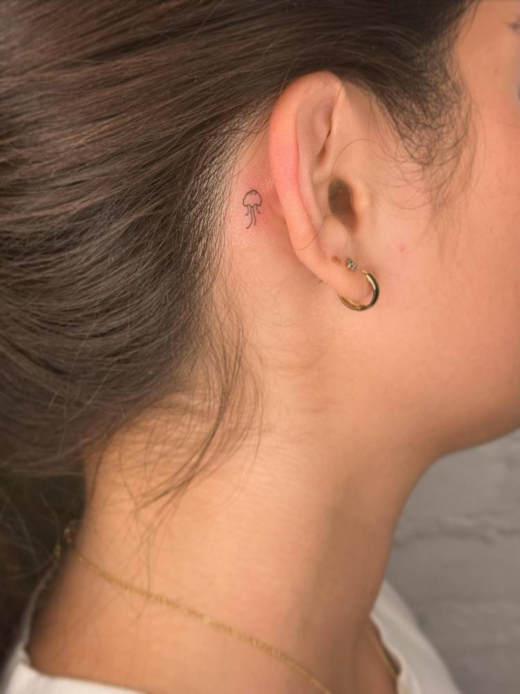 Micro jellyfish tattoo in minimalistic style placed behind the ear.