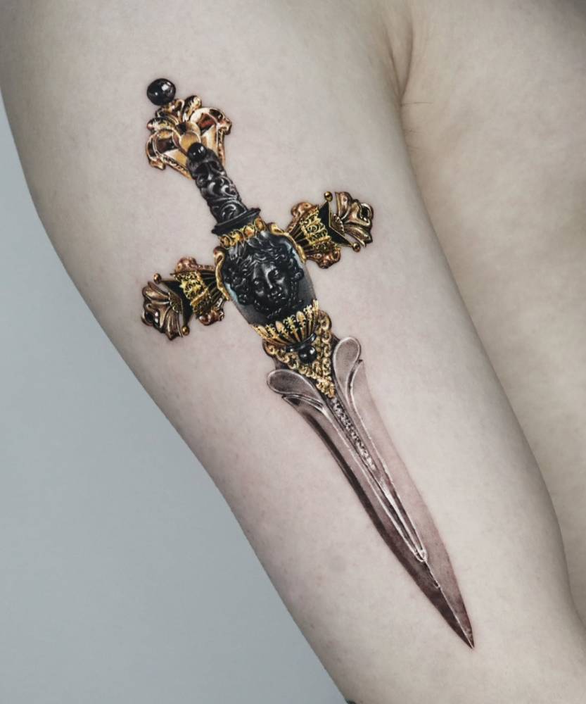 Dagger tattoo in realistic style located on the upper arm.