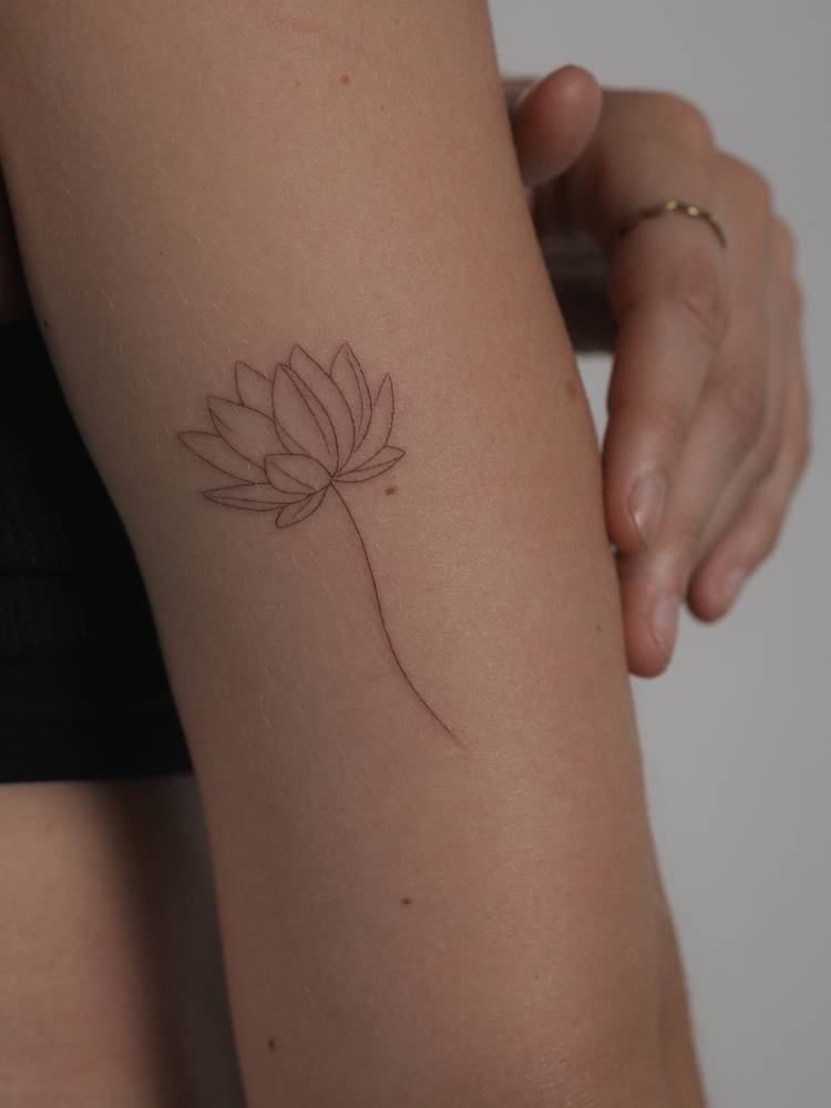 Lotus flower tattoo located on the tricep, done in fine line style.