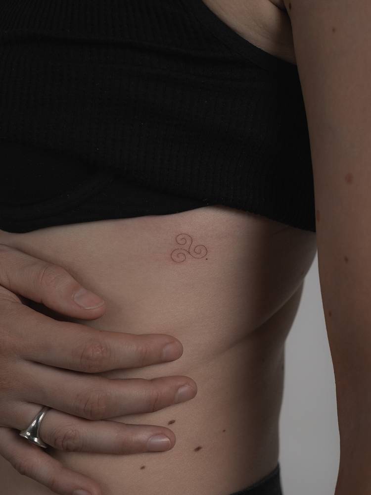 Minimalistic style triskelion tattoo placed on the rib.