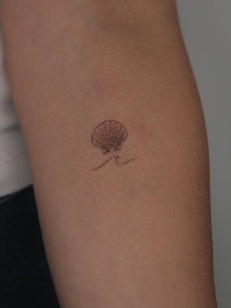 Scallop shell and wave tattoo located on the inner forearm.
