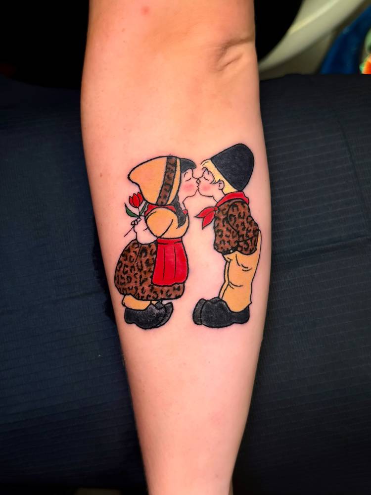 Kissing gnomes tattoo located on the forearm, cartoon style.