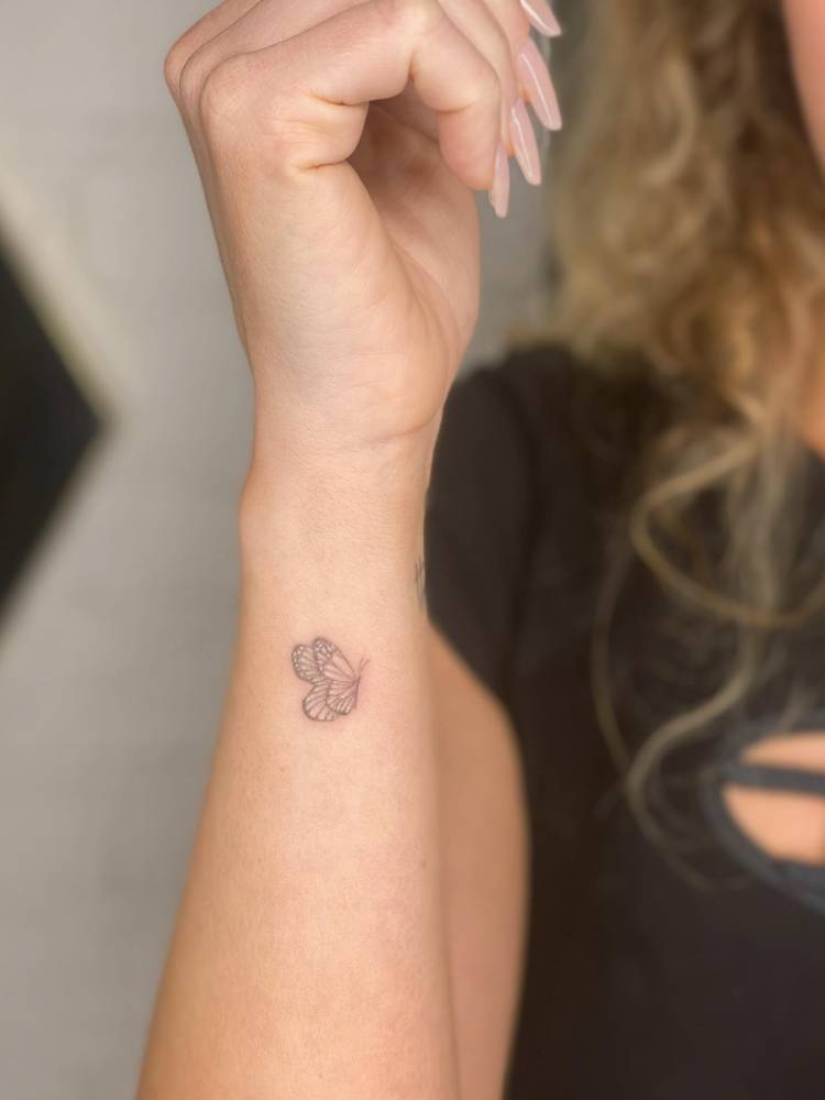 Fine line style butterfly tattoo located on the wrist.