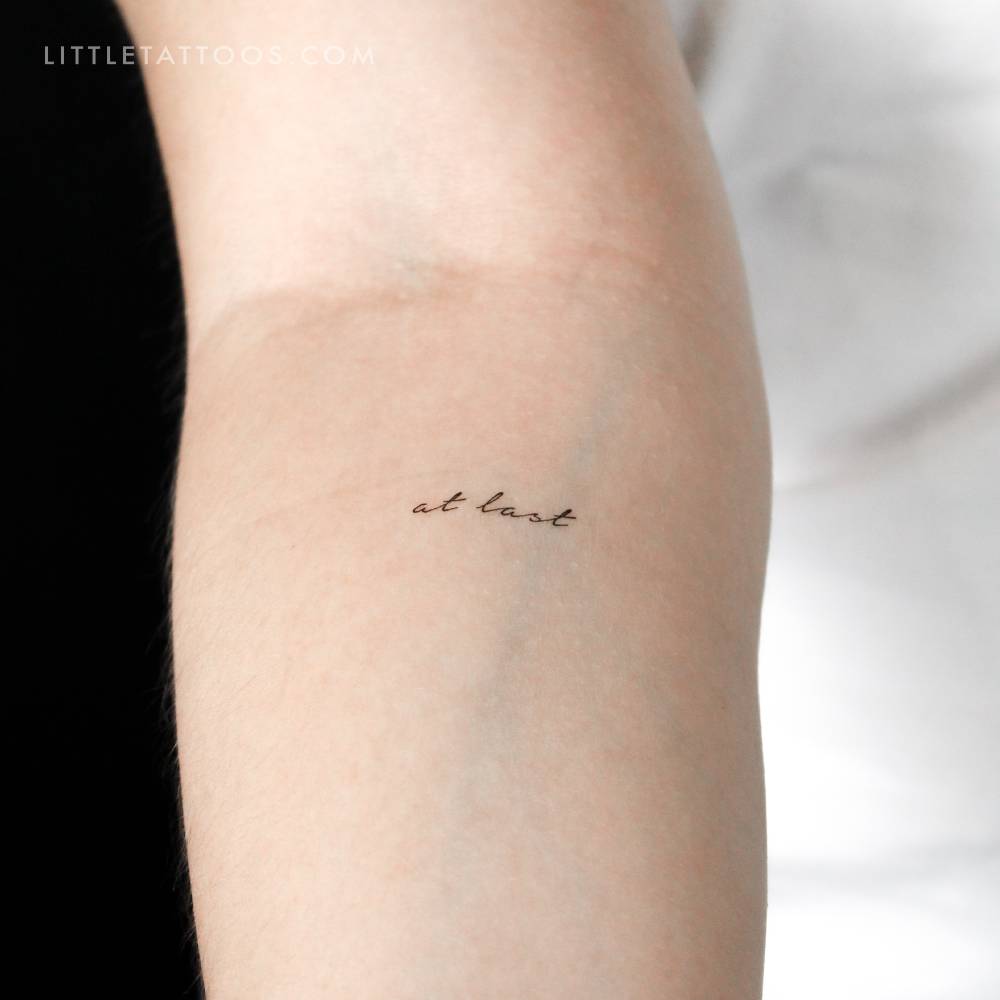 "At last" temporary lettering tattoo located on the inner forearm.