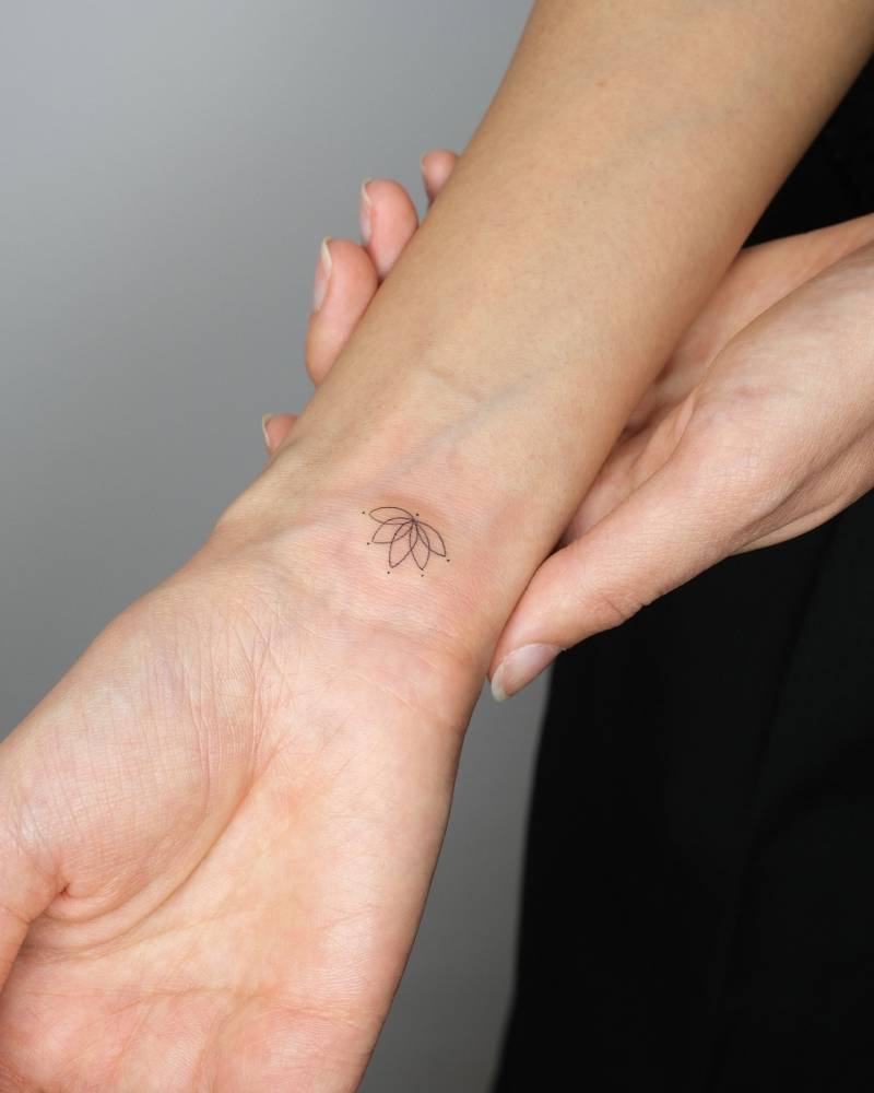 Tiny lotus flower tattoo in fine line style done on the wrist.