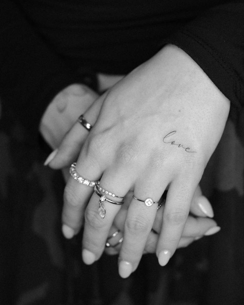 Script font word "love" tattoo located on the hand.