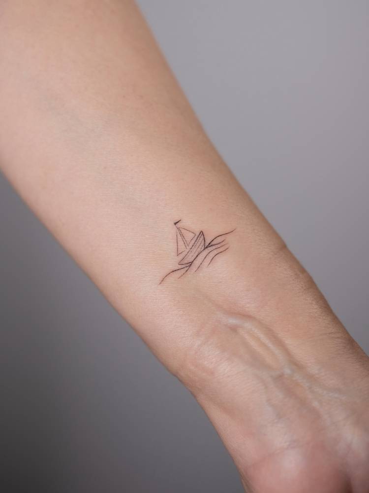 Sailboat tattoo in minimalistic style located on the wrist.