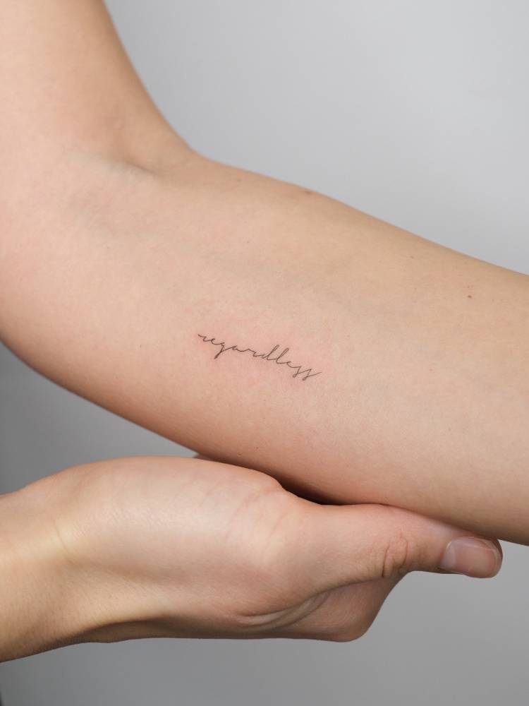 "Regardless" lettering tattoo in handwritten font located on the inner forearm.