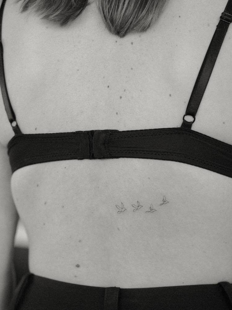 Tiny minimalistic flying birds tattoo located on the lower back.