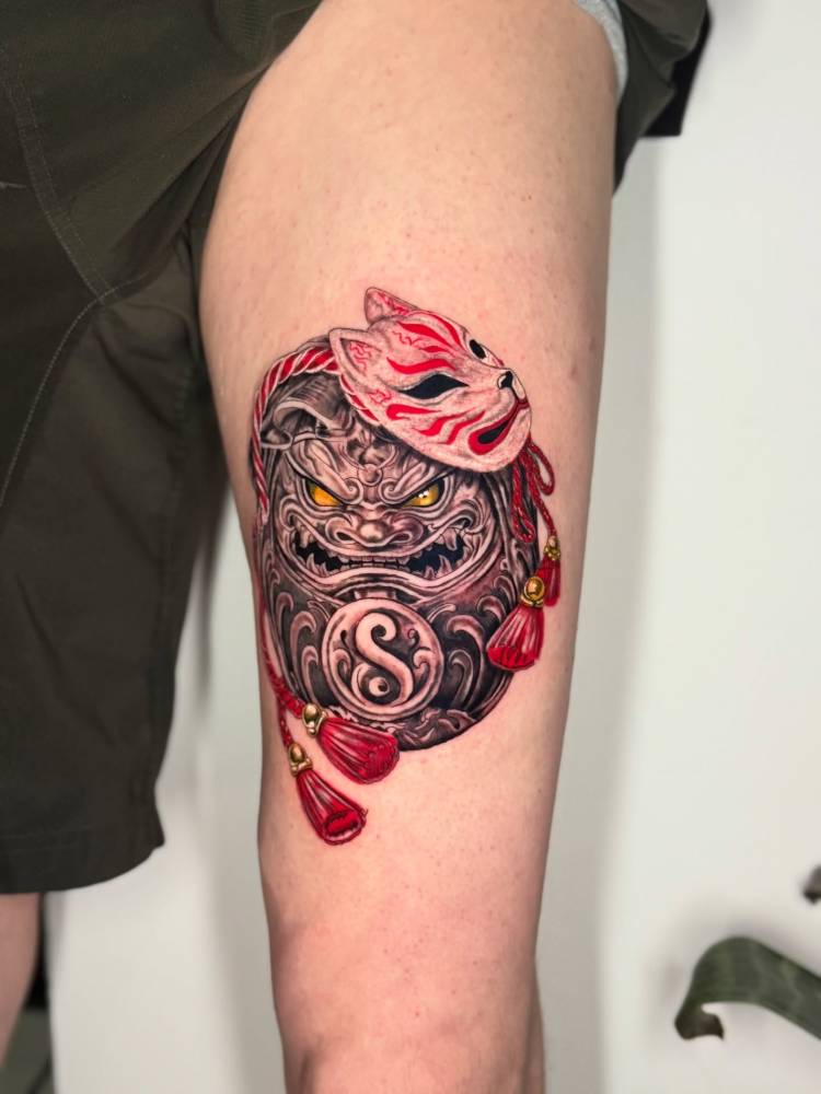 Daruma doll and kitsune mask tattoo located on the thigh.