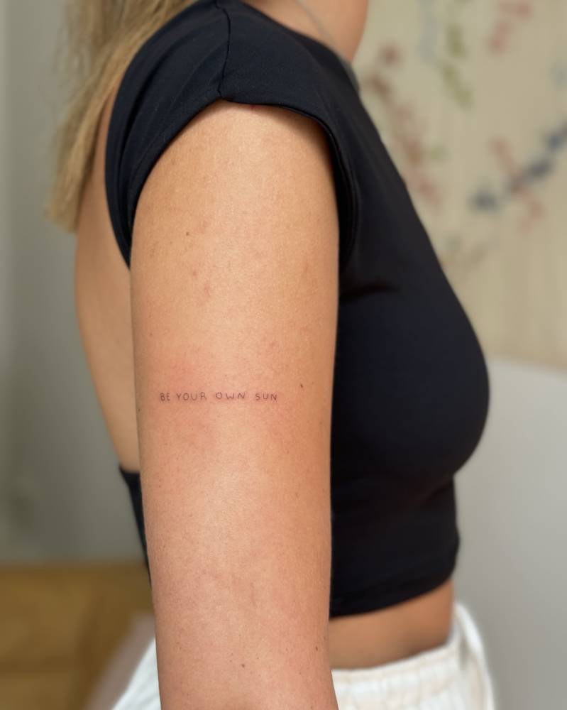 "Be your own sun" lettering tattoo placed on the upper arm.