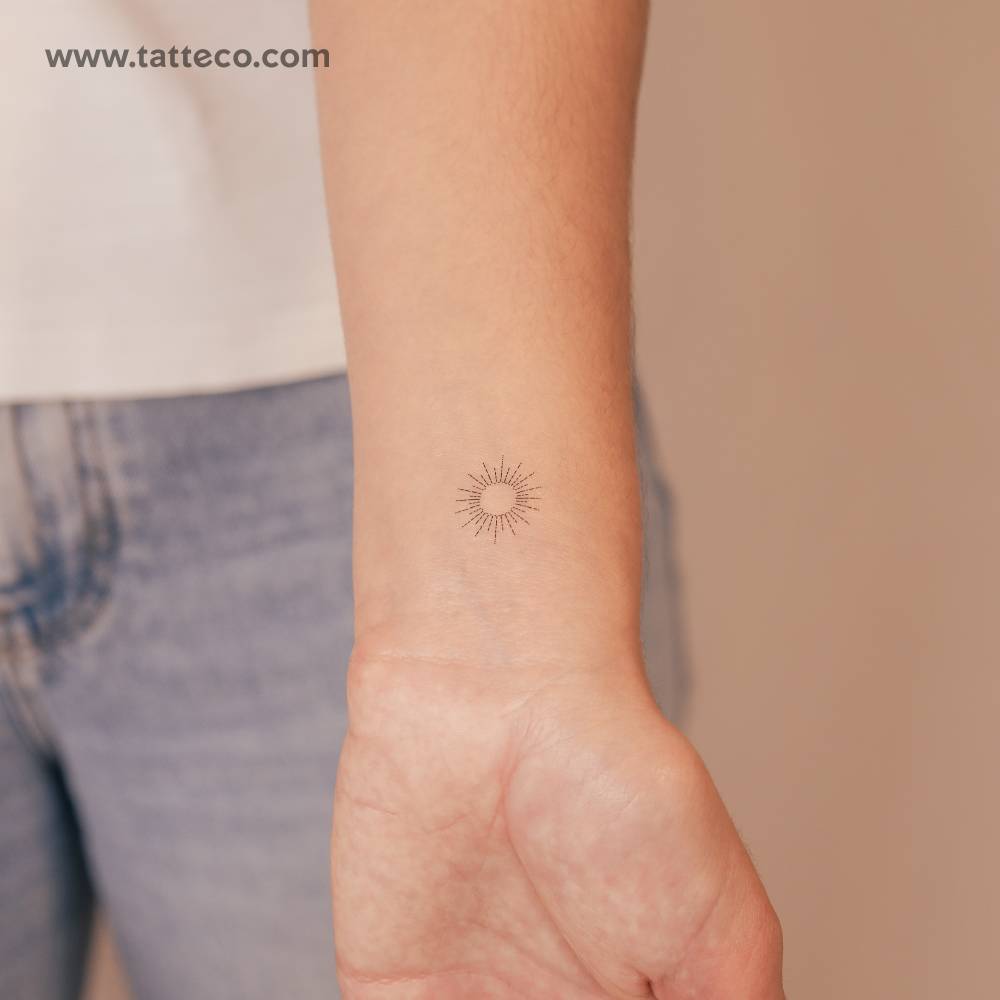 Fine line style tiny sun temporary tattoo placed on the wrist.