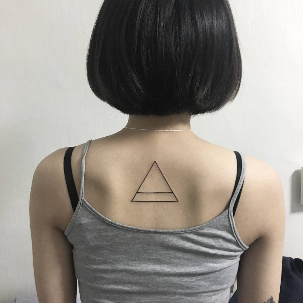 Minimalistic style triangle tattoo located on the upper back.