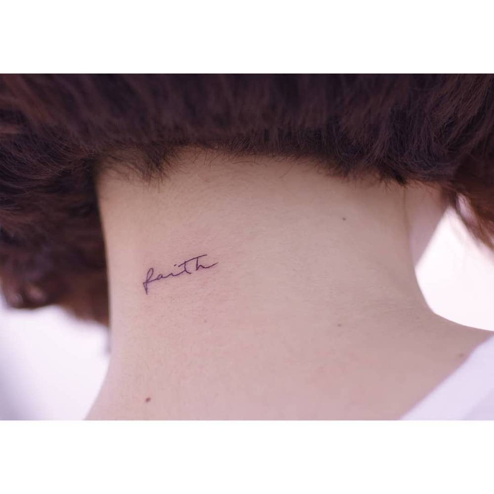 Little tattoo of the word "faith" in handwritten font located on the back of the neck.