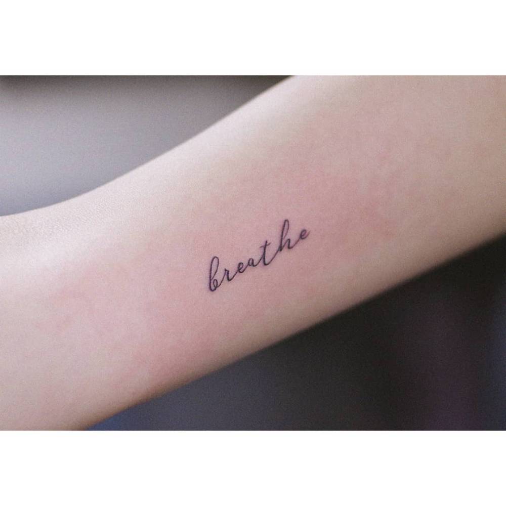 Handwritten font word "breathe" tattooed on the inner arm.