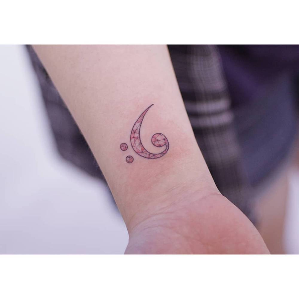 Illustrative style bass clef tattoo located on the wrist.