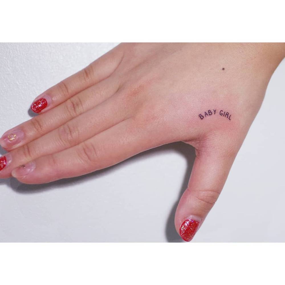 Lettering tattoo that says "baby girl" located on the hand.