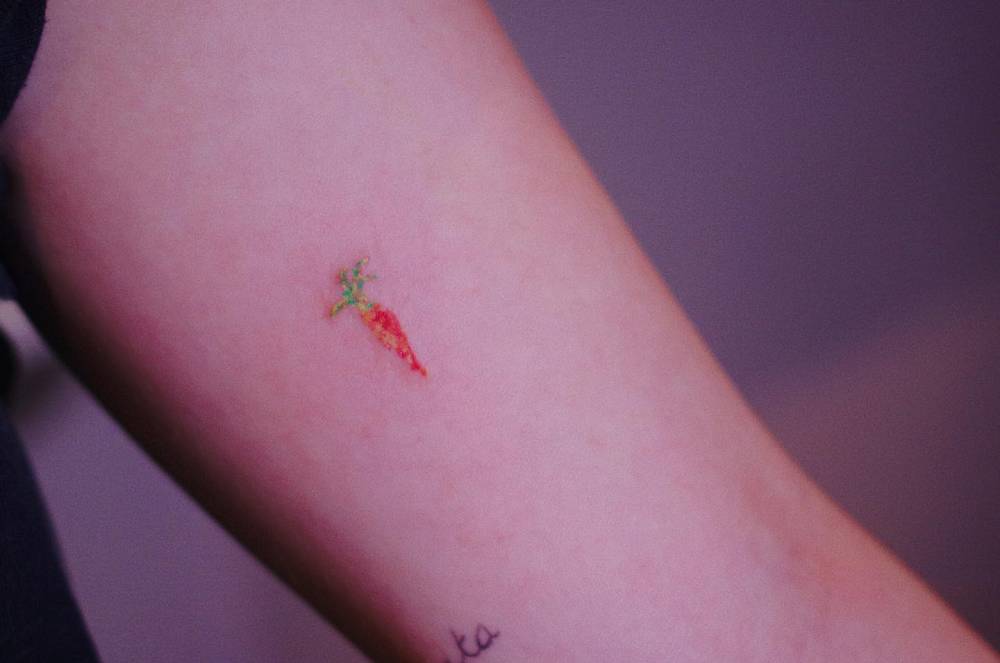 Tiny carrot tattoo in illustrative style placed on the inner arm.