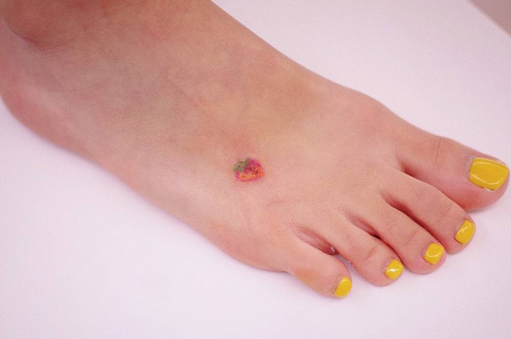 Tiny strawberry tattoo in watercolor style located on the foot.