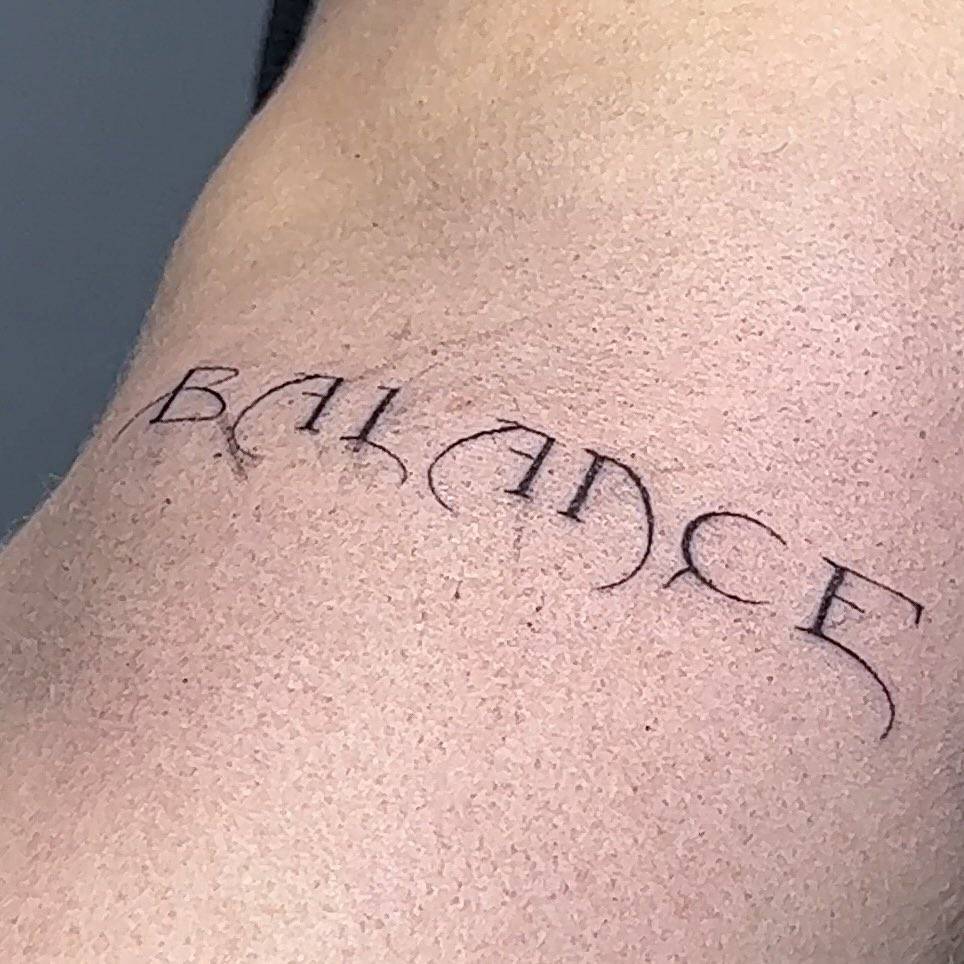 Tattoo of the word "balance" located on the upper arm.