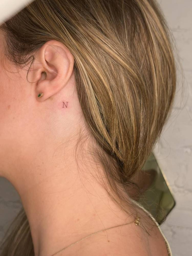 Typewriter font initial "N" tattooed behind the ear.