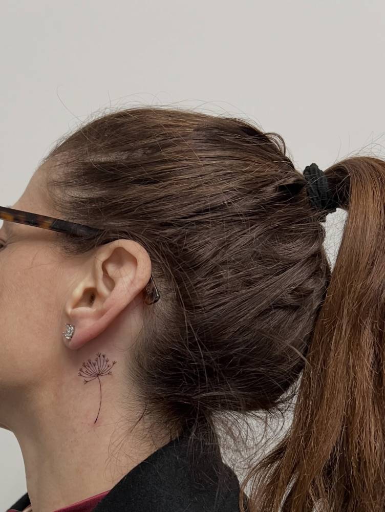 Fine line style dandelion tattoo located behind the ear.
