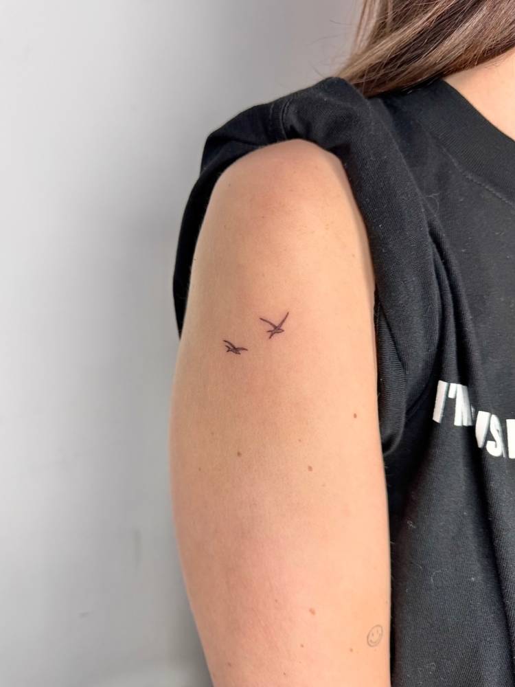 Flying birds tattoo in minimalistic style located on the upper arm.