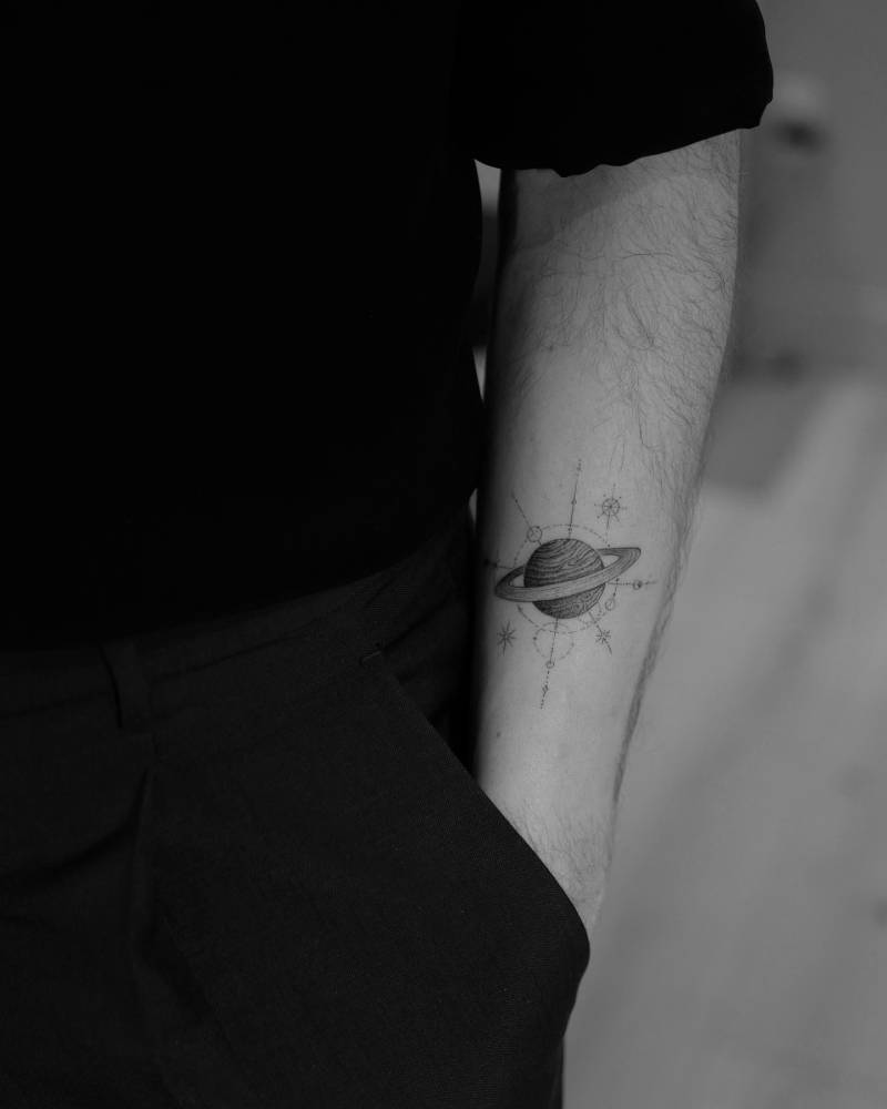 Single needle Saturn tattoo located on the inner forearm.