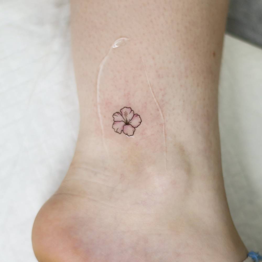 Minimalistic style hibiscus flower tattoo located on the ankle.