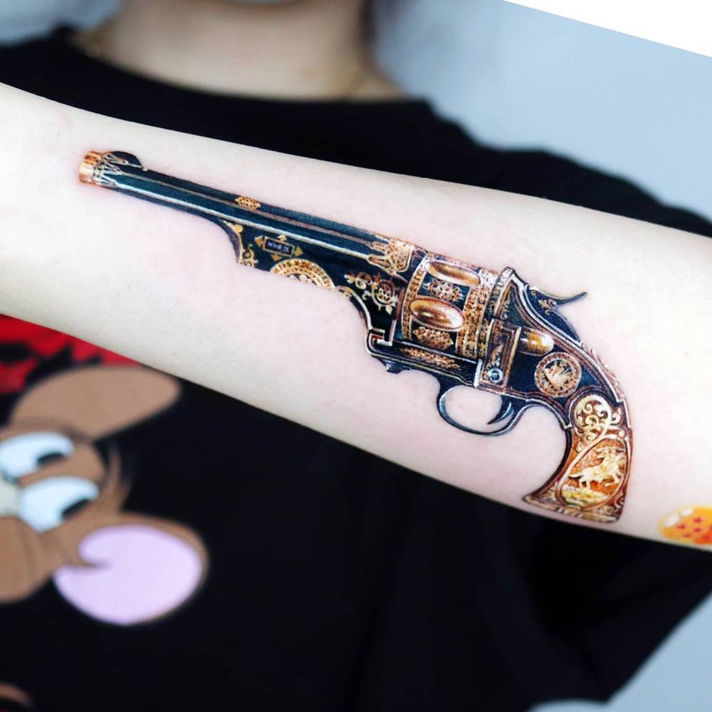 Micro-realistic style revolver tattoo located on the forearm.