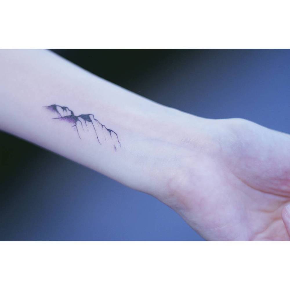 Mountains tattoo located on the wrist, illustrative style.