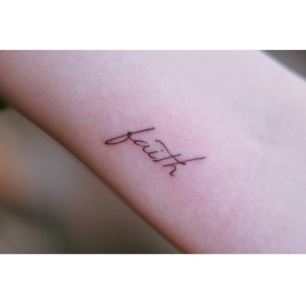 Word "faith" tattoo in handwritten font located on the inner arm.