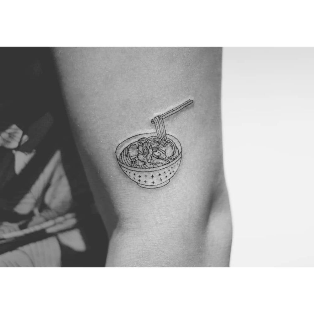 Ramen tattoo located on the upper arm, illustrative style.