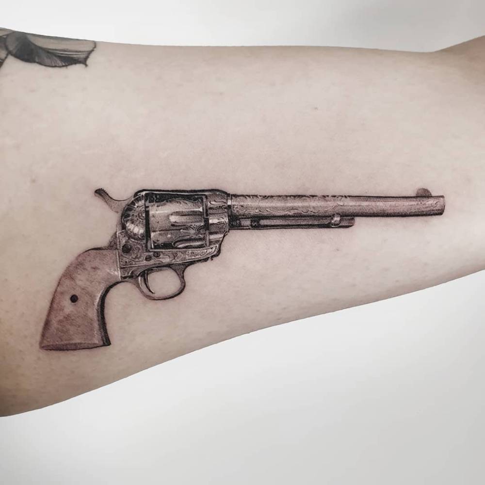 Revolver tattoo located on the inner arm, micro-realistic style.
