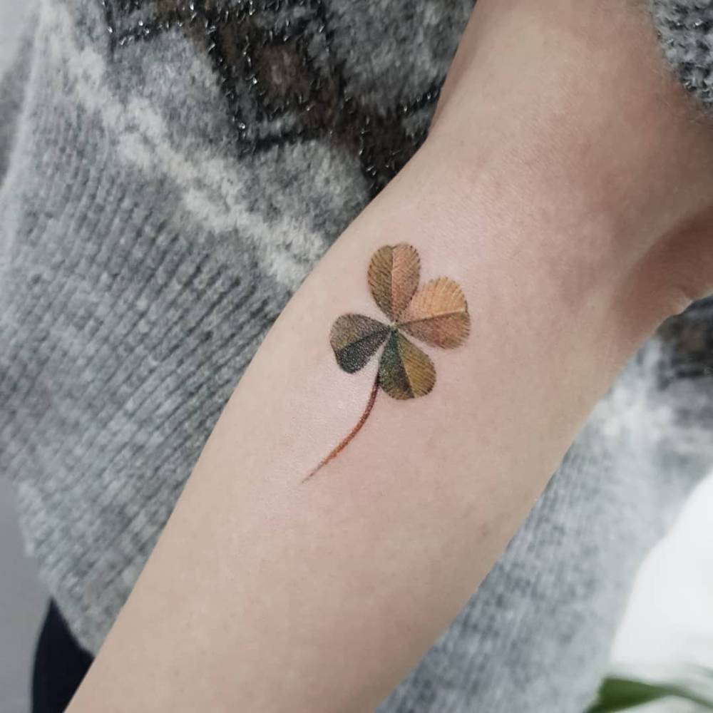 Micro-realistic style four leaf clover tattoo located on the forearm.