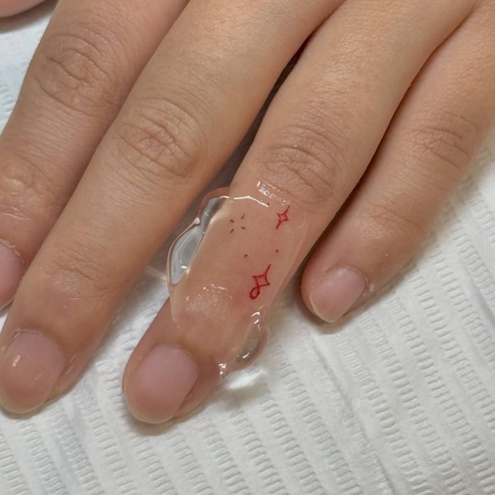 Tiny minimalistic sparkling stars in red ink tattooed on the finger.