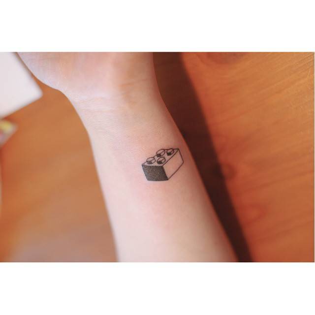 Lego brick tattoo in illustrative style located on the wrist.