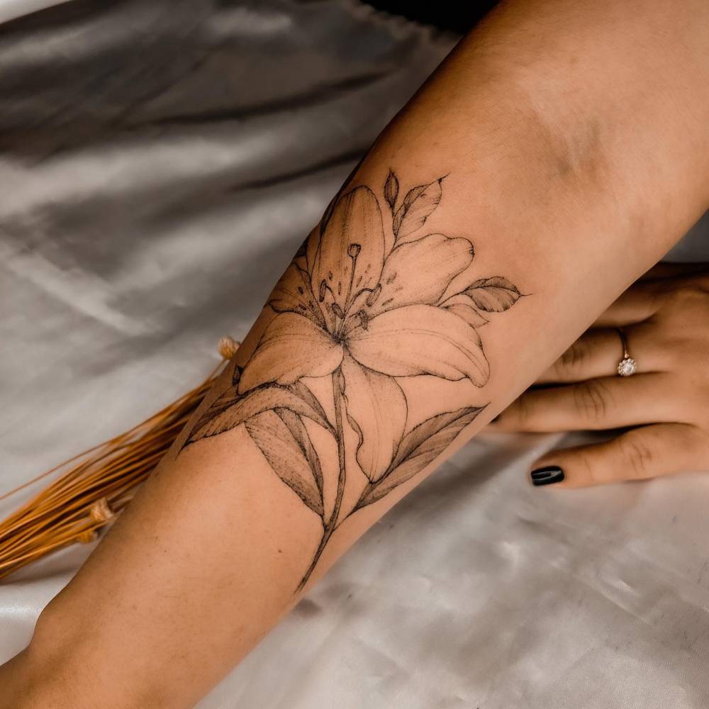 Lily flower tattoo placed onm the forearm, illustrative style.