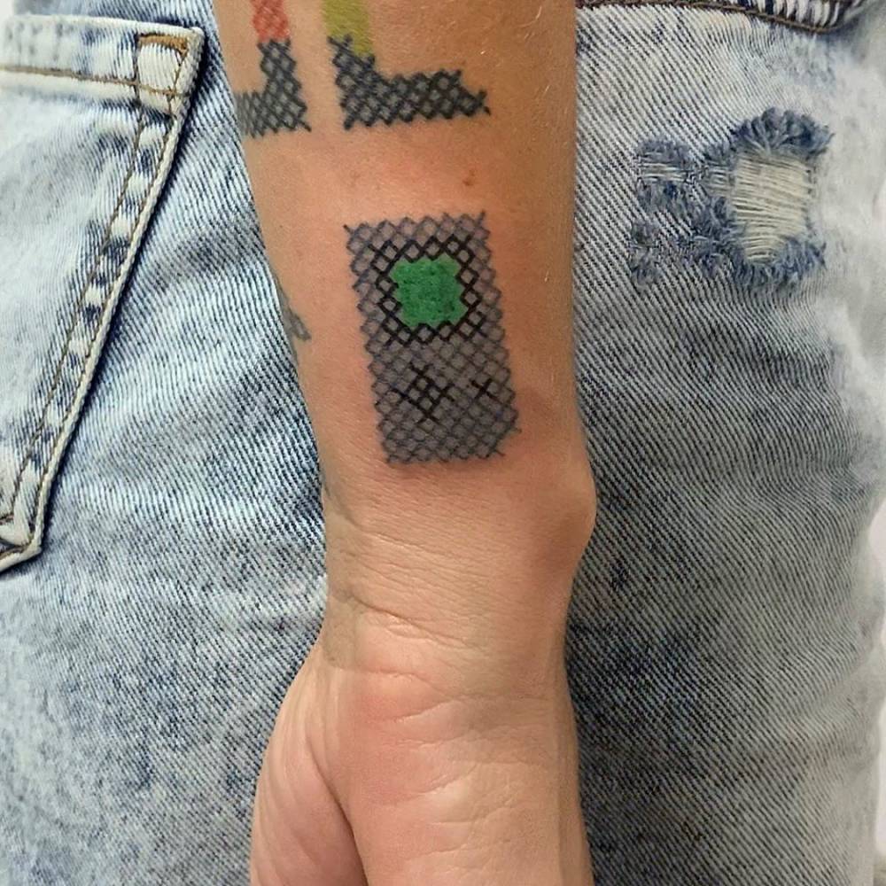 Game Boy tattoo located on the wrist, cross stitch style.