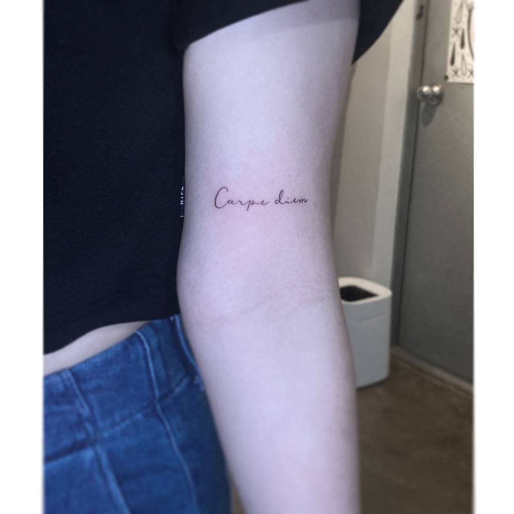 Handwritten "carpe diem" lettering tattoo located on the bicep.