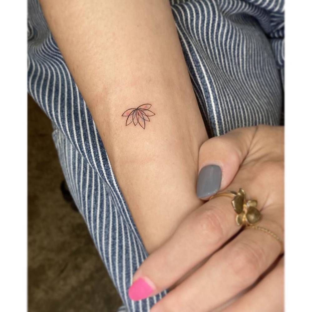 Little lotus flower tattoo in illustrative style located on the inner forearm.