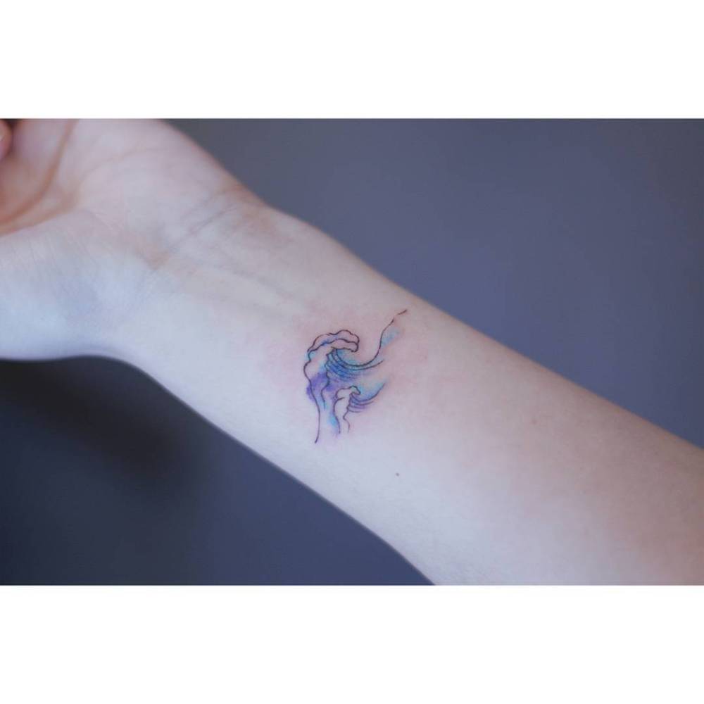 Watercolor style wave tattoo located on the wrist.